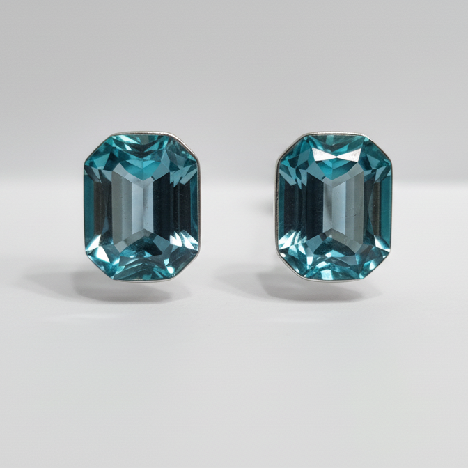 Two emerald-cut blue gemstones earrungs on a light gray background