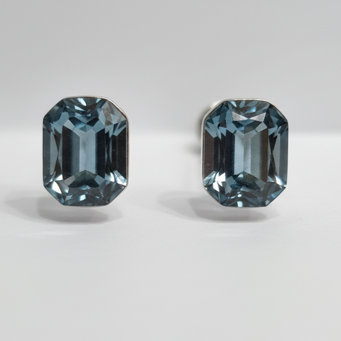 Two emerald-cut blue gemstone searrings on a light gray background