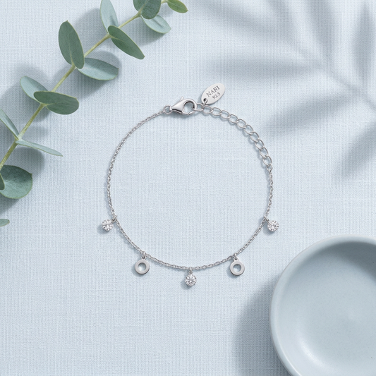 Tempo Charm Silver Bracelet flatlay on pale linen with eucalyptus