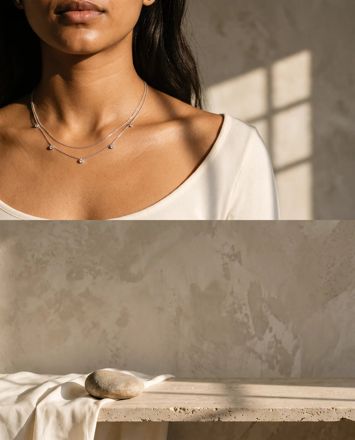 Vertical crop of the same scene: a woman photographed from the lips down wearing a layered 925 sterling silver chain necklace, against a sunlit warm plaster wall with a travertine ledge, ivory silk and a river stone below.